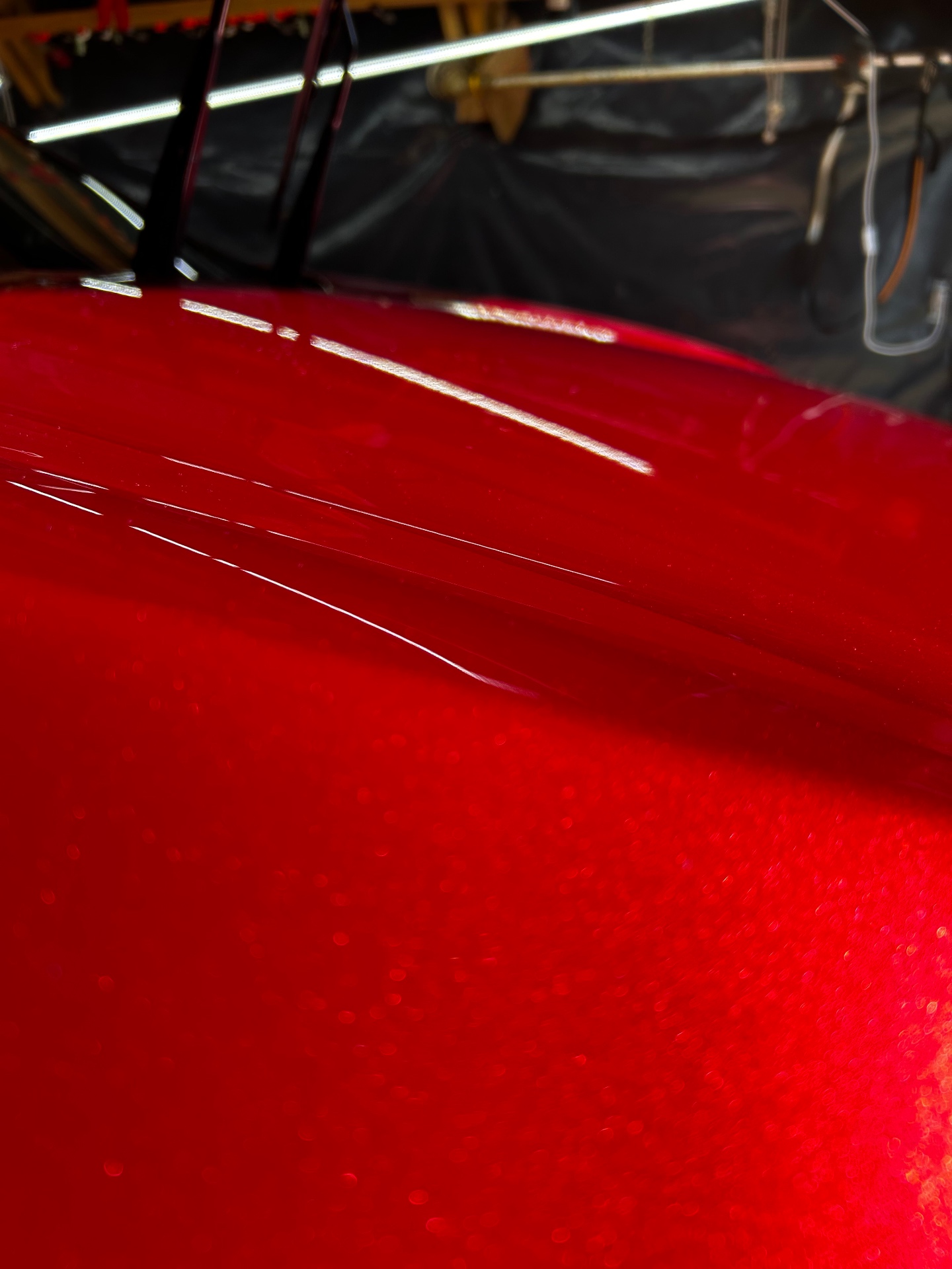 High-angle close-up of a glossy metallic red hood with bright overhead light reflections
