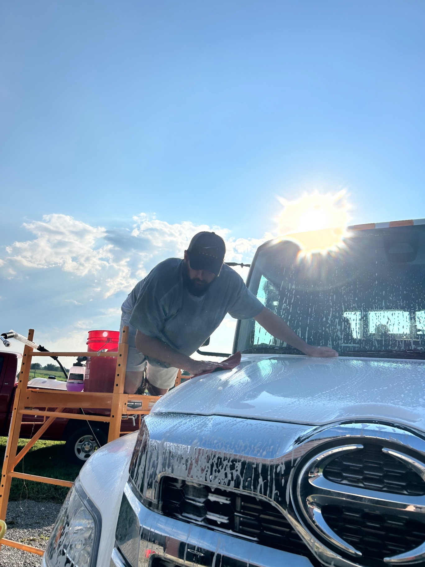 Detailer hand washing a foamed truck hood in the sun