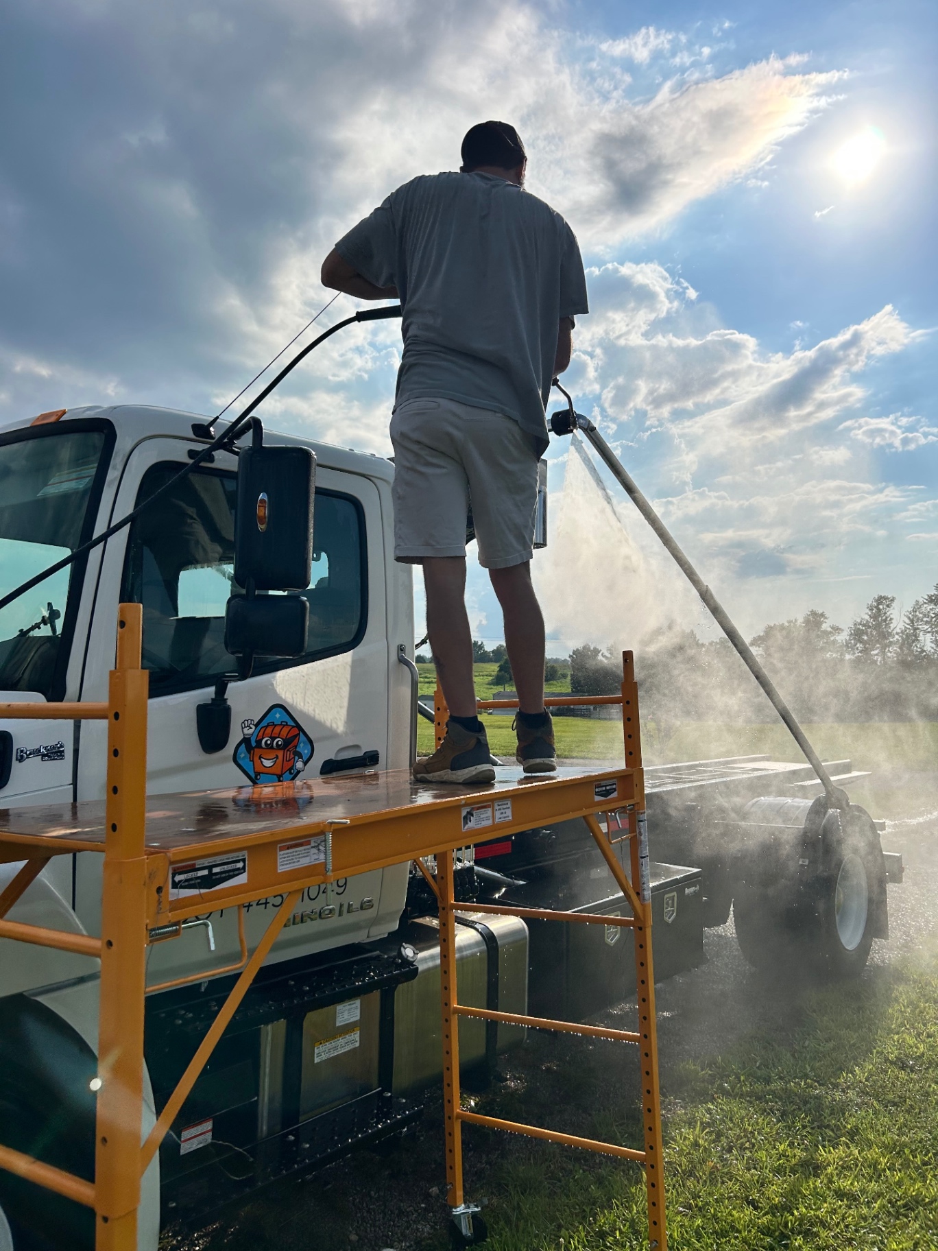 Detailer pressure rinsing the roof of a work truck from scaffolding