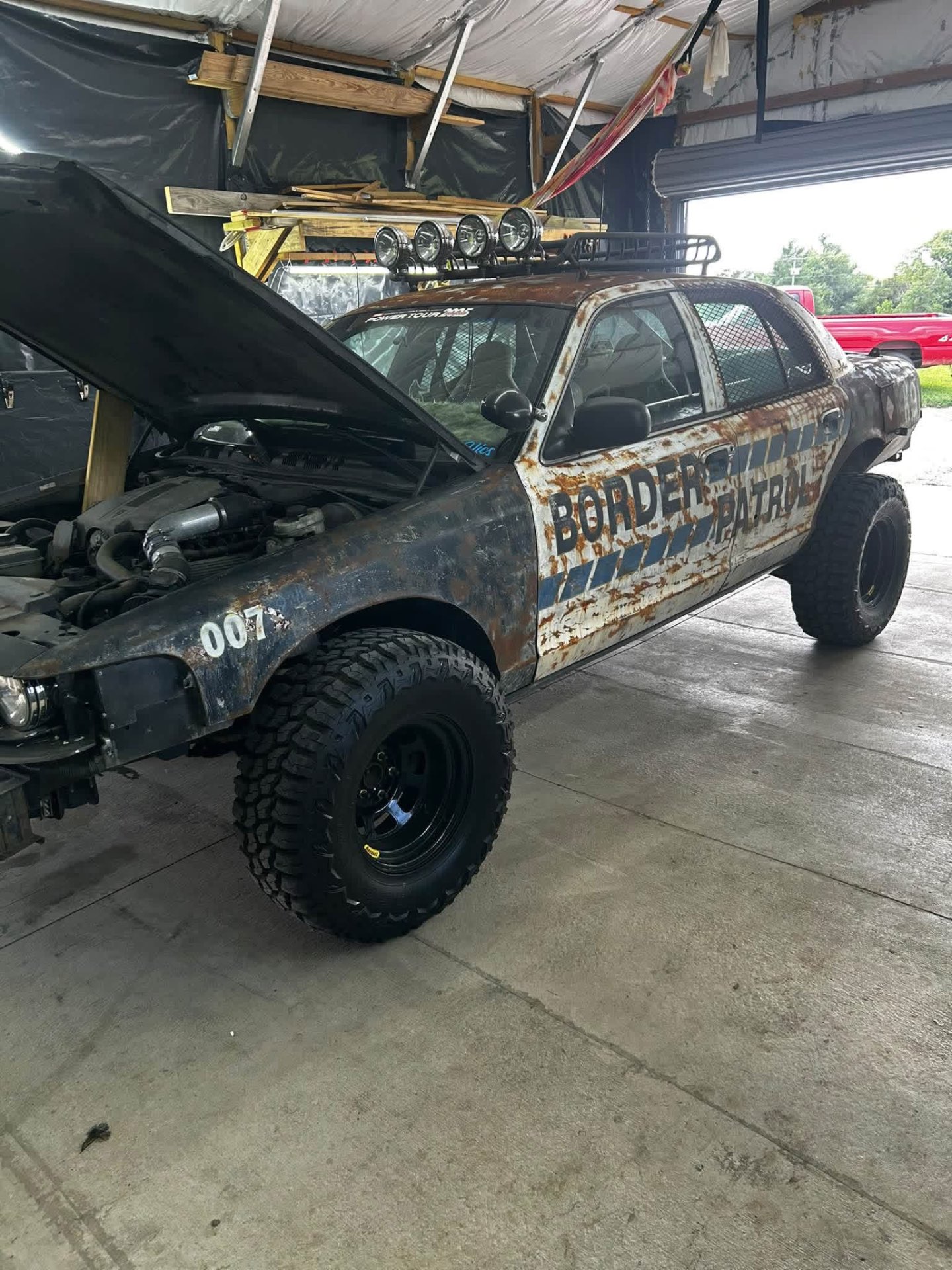 Rusted Border Patrol project car with hood open in the shop