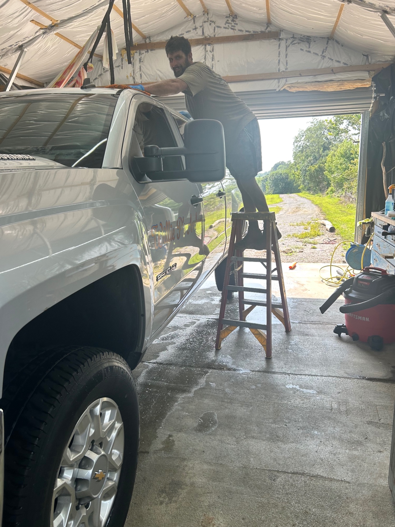 Detailer on a ladder hand drying the roof of a silver truck