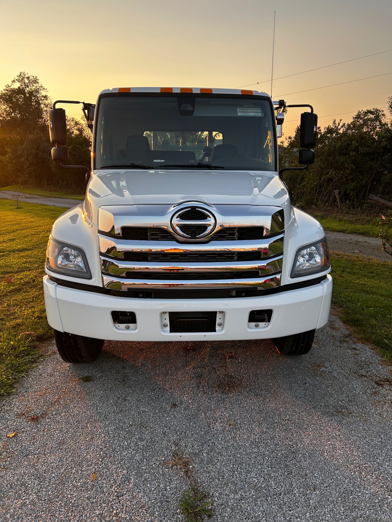 Front view of a white Hino truck with polished chrome grille at sunset